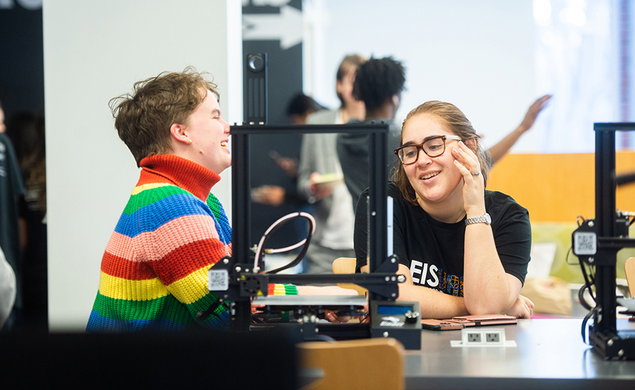 Students laugh while operating a 3D printer.