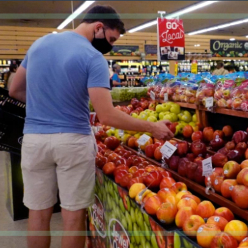 A man examining a display of apples in a grocery store.