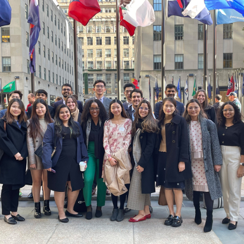 Students pose in front of a row of flags outside Deloitte's New York office.