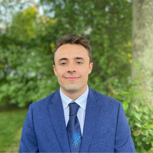 A portrait of Alex Losada in a blue suit with trees in the background.