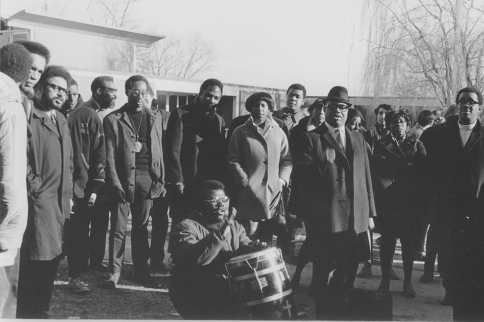 Black students stand in a group, with one student playing a drum in the center.