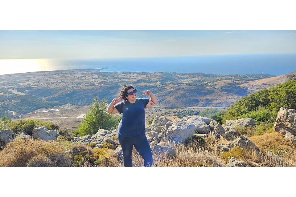 Alexandra Burkot poses on a mountaintop, making two muscles.