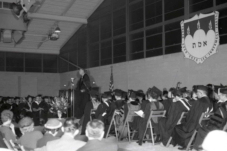 GSAS students, in robes, sit listening to a convocation speaker.