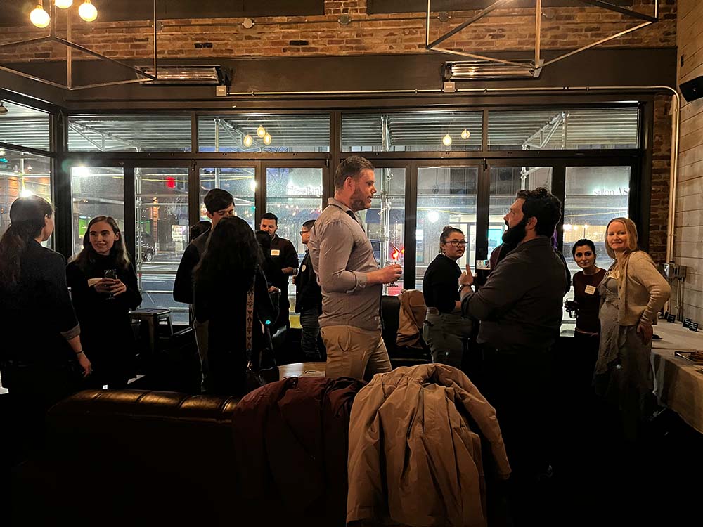 GSAS students and alums talk in small groups amongst restaurant tables and chairs.