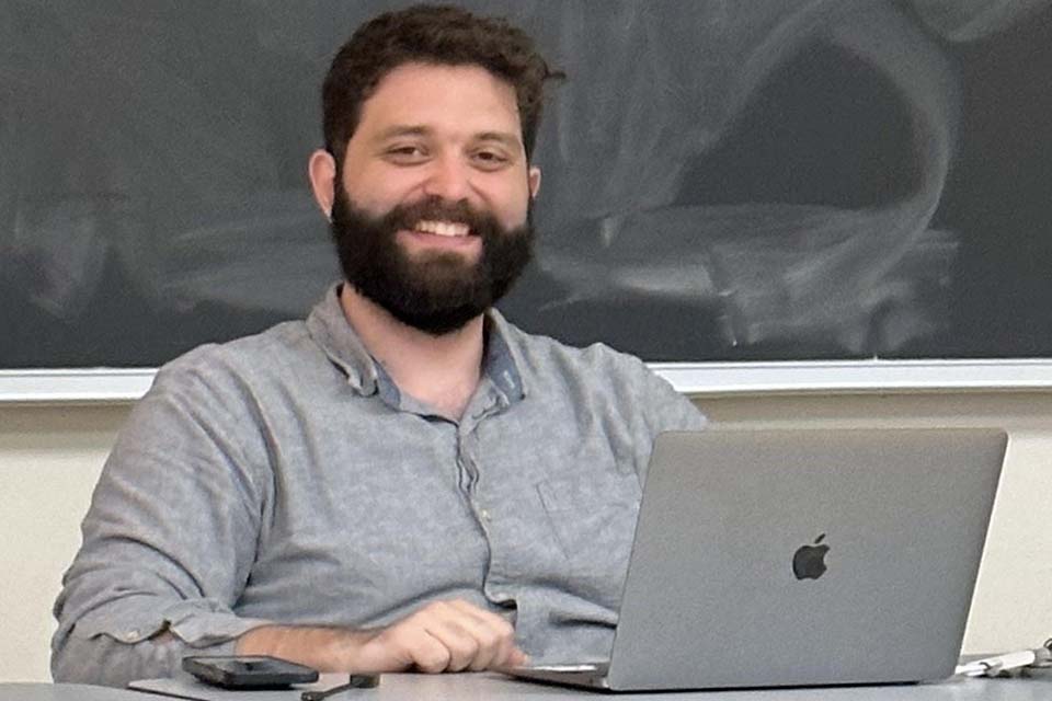 Mike Vivian sits with a laptop in front of a blackboard.