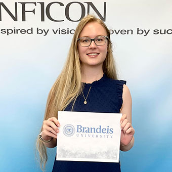 Annika Sparrell standing in front of an Inficon backdrop, holding a paper that says "Brandeis University"
