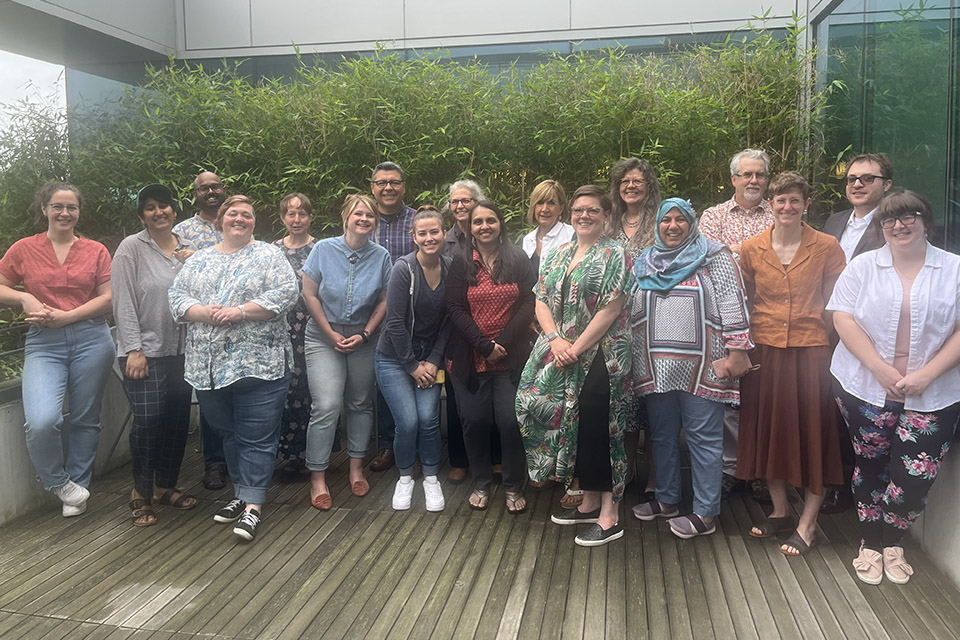 Twelve participants in the reading-writing pedagogy institute pose in two lines in front of greenery.