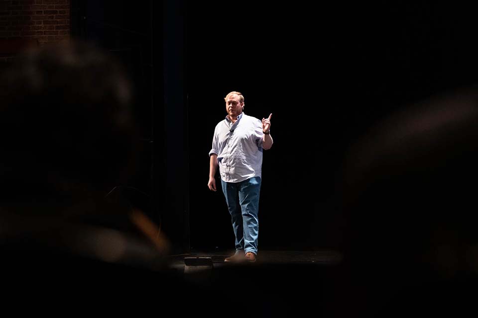 Will Dahl stands on a stage speaking during the 3MT competition.