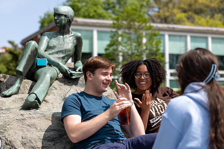 From right, Elienne Grossman, ’26, Lola Hamilton, ’26, Mikey Terrenzi, ’25, hang out beside the Student and Knowledge sculpture outside of the Brandeis University libraries on May, 9 2023.Photo/Gaelen Morse