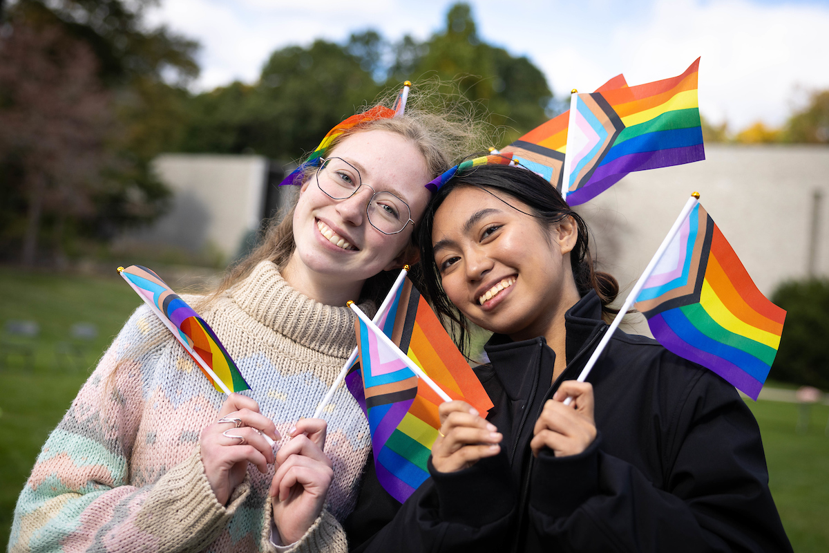 Two students pose for photo holding Pride flags.