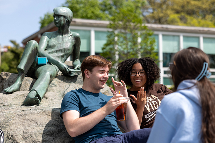 From right, Elienne Grossman, ’26, Lola Hamilton, ’26, Mikey Terrenzi, ’25, hang out beside the Student and Knowledge sculpture outside of the Brandeis University libraries on May, 9 2023.Photo/Gaelen Morse