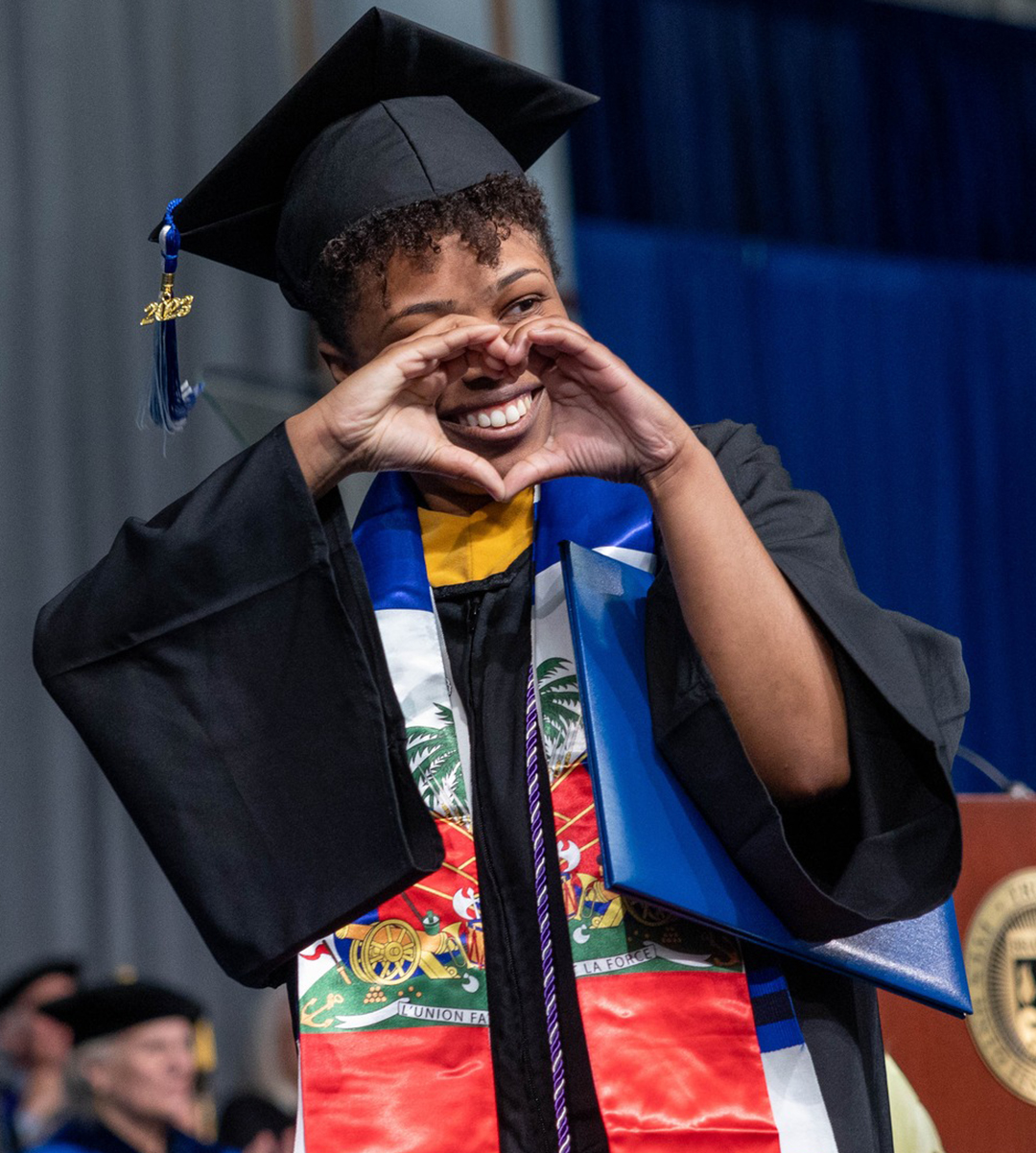 Brandeis University student speaker Nathalie Vieux-Gresham makes the shape of a heart to her fellow graduates after walking across the stage during the undergraduate Commencement ceremony at the Gosman Sports and Convocation Center.