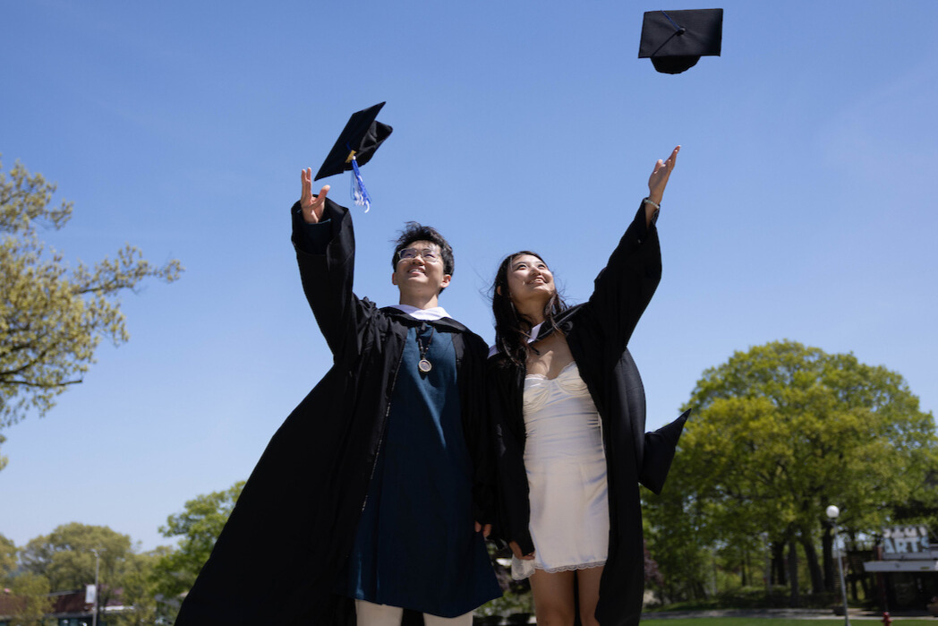 Two students toss graduation caps on Brandeis campus.