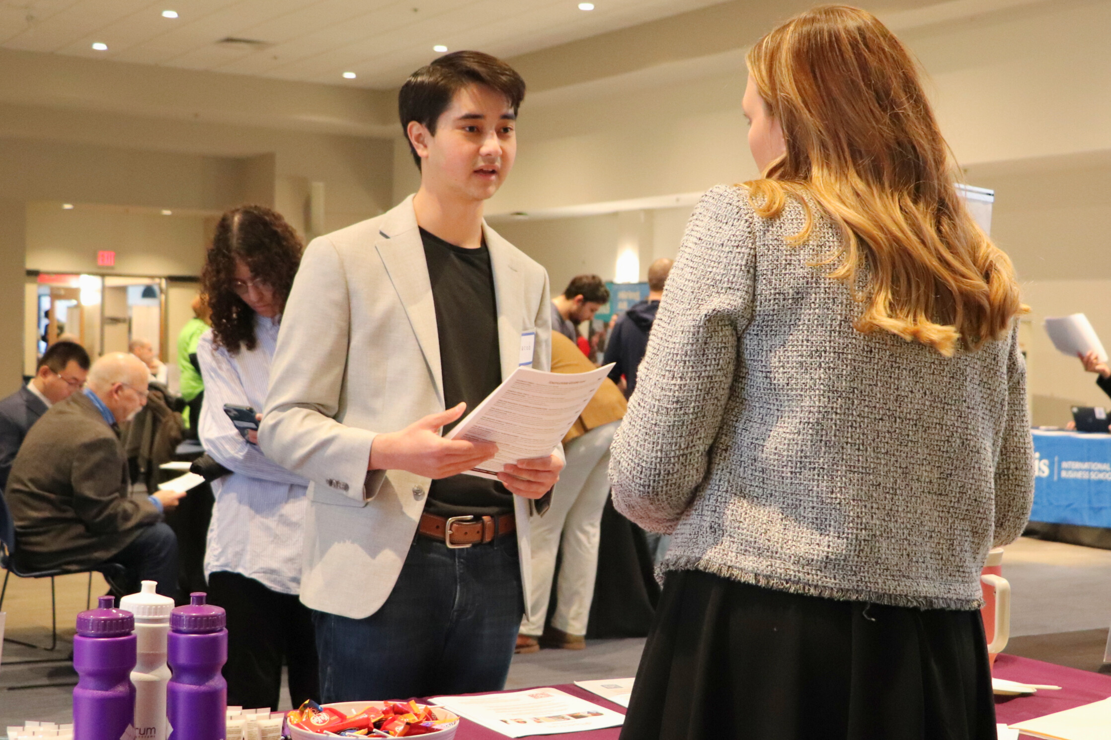 Student holds resume and speaks to employer at career fair.