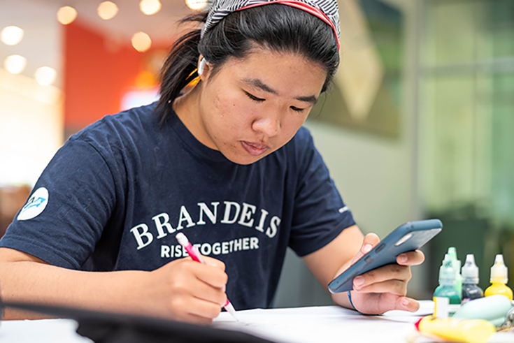 Emily Su ’23, sketches out a design she will use to adorn her mortarboard for her upcoming commencement ceremony during a graduation cap decoration event at the Shapiro Campus Center on May 16, 2023. Photo/Gaelen Morse