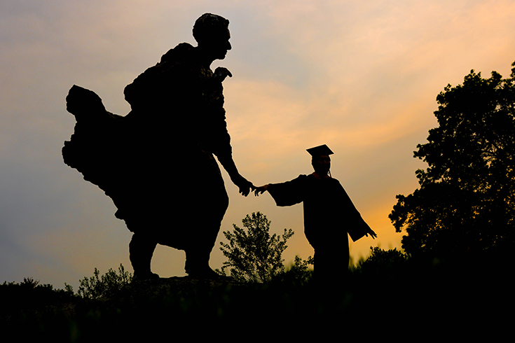 Jack Yuanwei Cheng ‘23 poses for a photo in his graduation regalia with the Louis Brandeis statue at Brandeis University on May 16, 2023. Photo/Dan Holmes