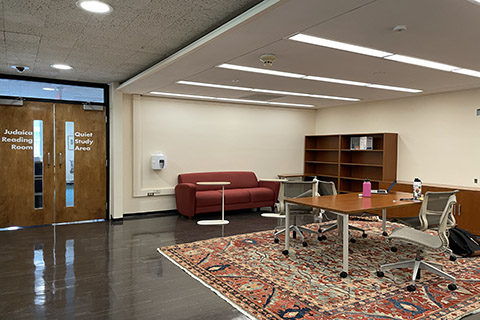 A room within the library with a red couch, a seminar table with several chairs, bookshelves, and a read carpet. 