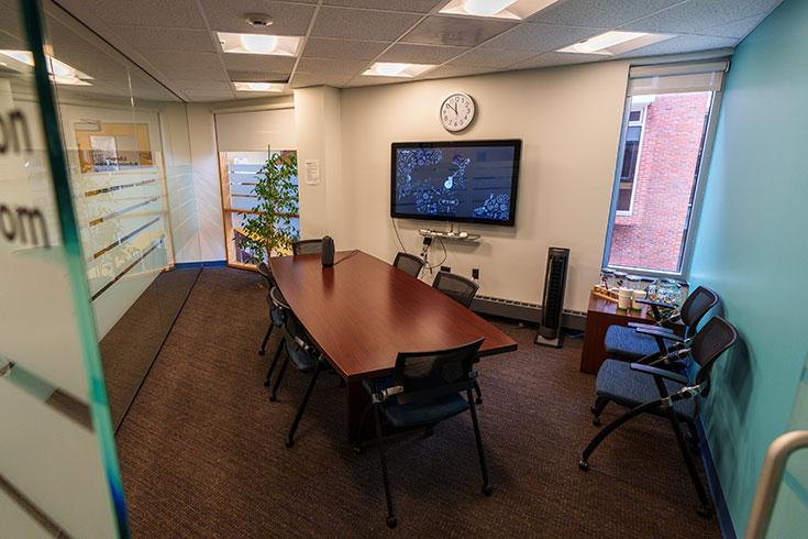 A room with a conference table and a T.V. mounted on the wall