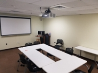 A room with a projector and a large table surrounded by chairs