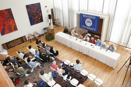 An aerial view of a large room filled with an audience sitting in chair watching speakers
