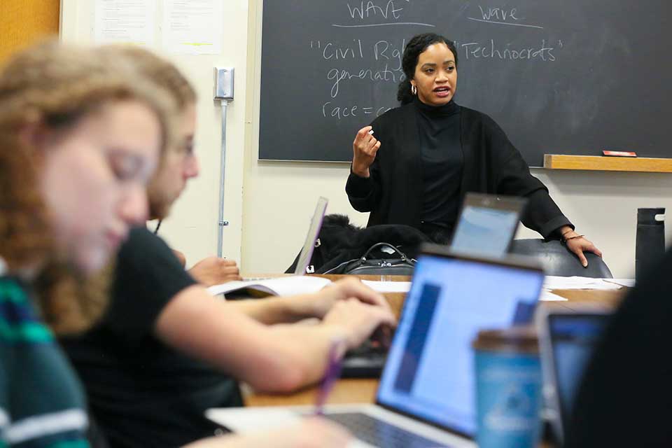 A faculty member teaches in front of students with laptops
