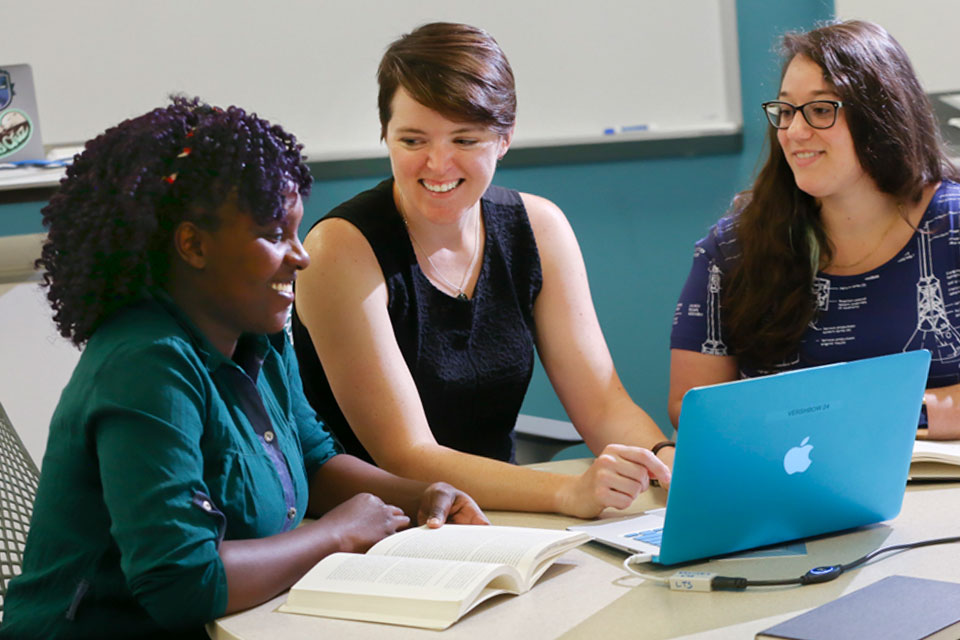 An instructor seated at an open laptop with two other people with open books