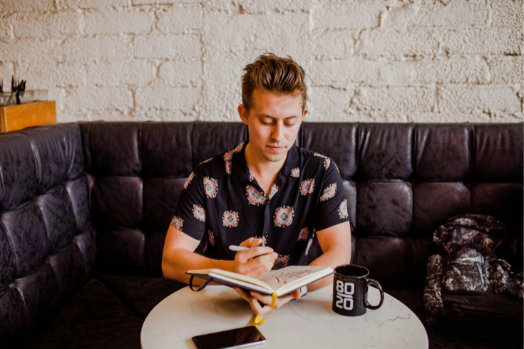 Person looking at a laptop with a notebook and pen in hand.