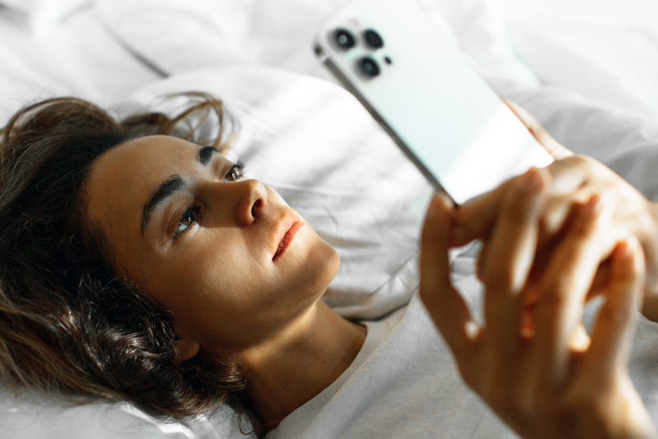A person lays on a bed looking at their cell phone