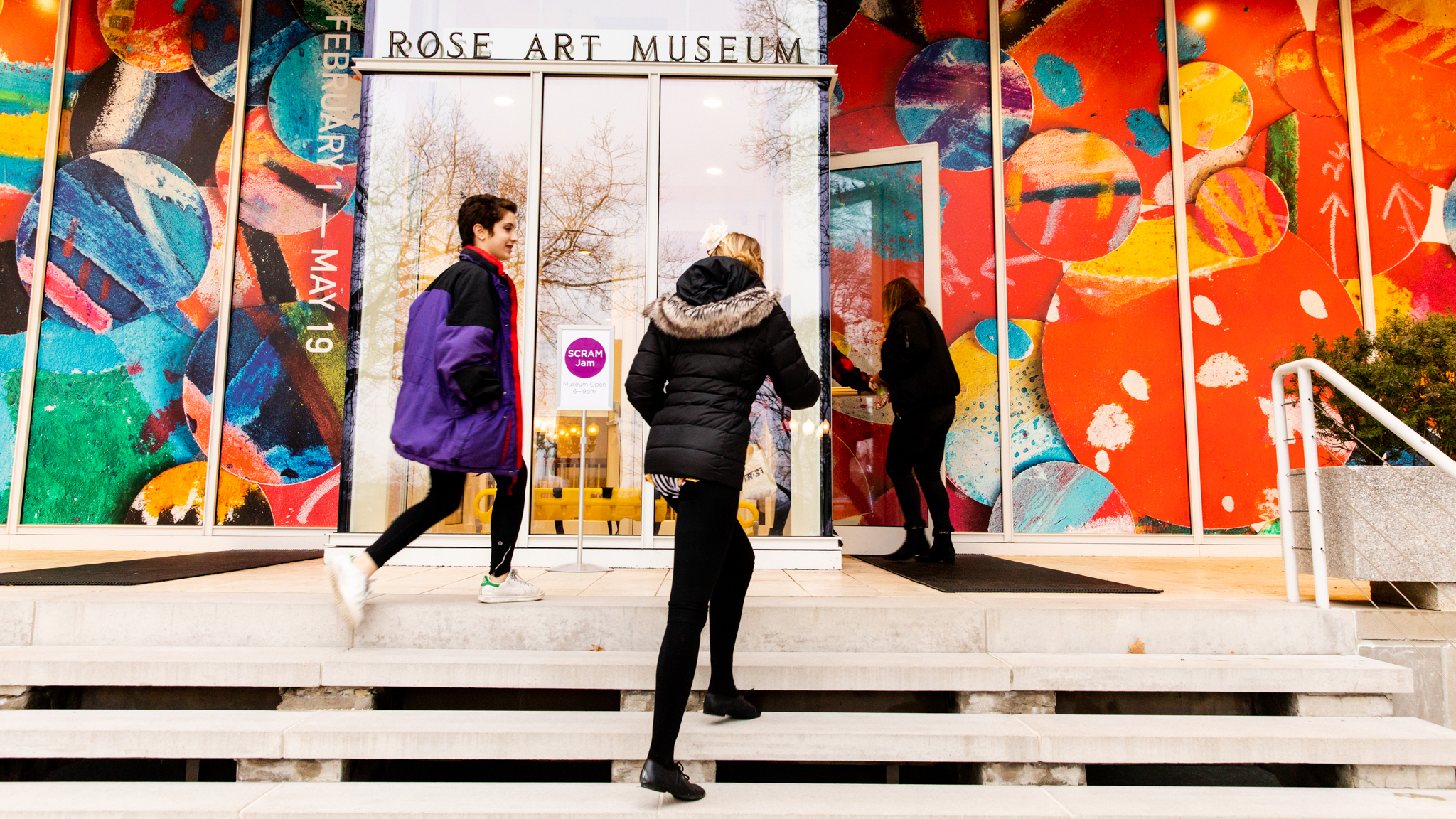 three people running up the front steps of the Rose Art Museum