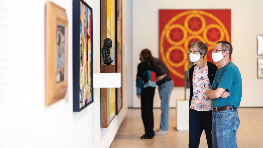 A woman and a man wearing face masks, looking at a painting.