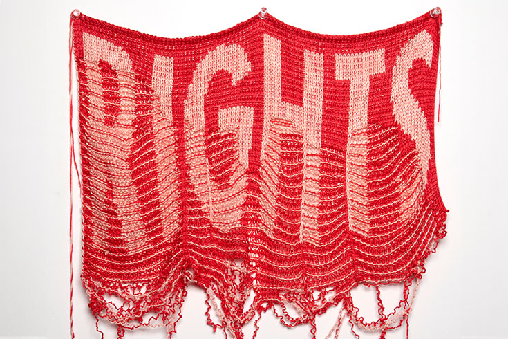A piece of unraveling knit cloth with the words "Rights" knit into the cloth